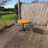 Moderne ronde cafétafel voor buiten met houten blad en groene designstoelen op een ruim houten terras.