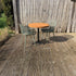 Terrasmeubelset met compacte ronde tafel, zwart onderstel en twee groene stoelen op een houten vlonder in de tuin.