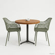 Ronde horecatafel met een tafelblad in Warm Brown kleur, gecombineerd met twee groene designstoelen met open rasterstructuur en een zwart metalen onderstel in een strakke, minimalistische setting.