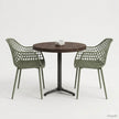 Ronde horecatafel met een tafelblad in Rich Brown kleur, gecombineerd met twee groene designstoelen met open rasterstructuur en een zwart metalen onderstel in een minimalistische studio-opstelling.