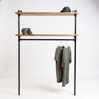 Industriële kledingkast van zwart staal met twee legplanken van bruine vurenhout, op een witte achtergrond met hangende T-shirts, boots en pet.