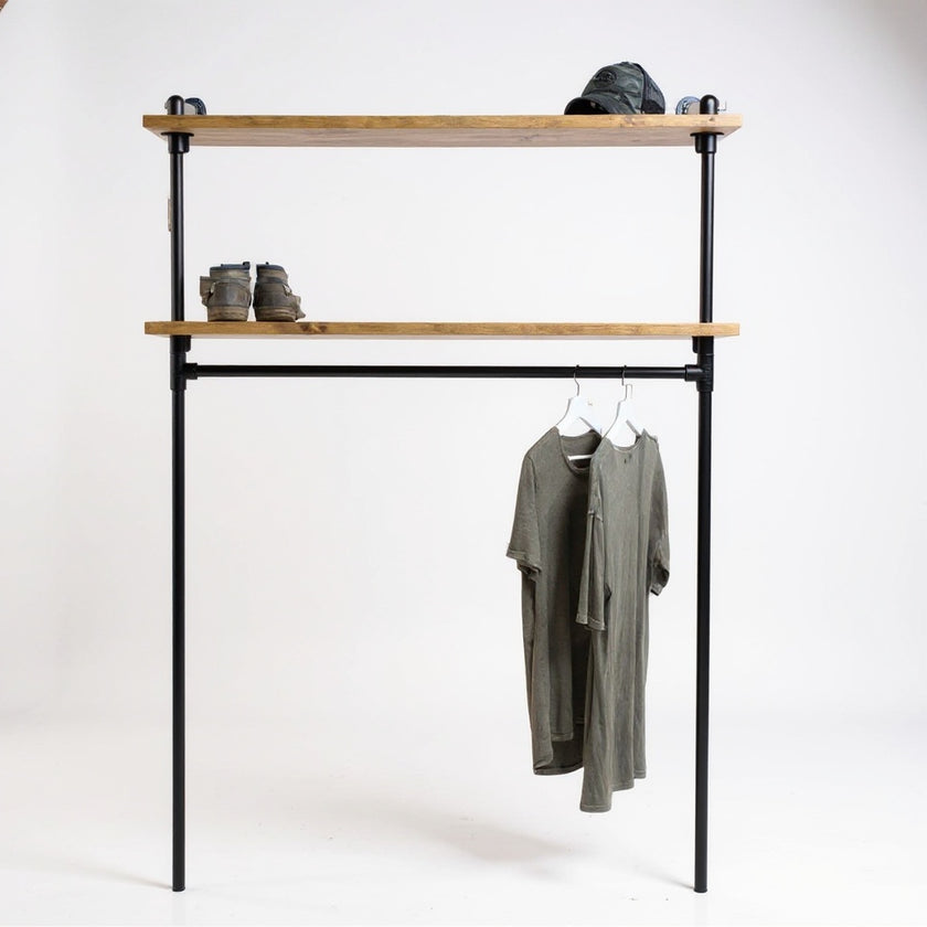 Industriële kledingkast van zwart staal met twee legplanken van bruine vurenhout, op een witte achtergrond met hangende T-shirts, boots en pet.