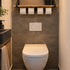 Industriële WC rolhouder Stijlvol van zwart staal met houten plank en vier toiletrollen, aan de muur gemonteerd boven een modern wit toilet in een sfeervolle toiletruimte.