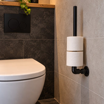 Industriële WC Rolhouder van zwart staal met twee toiletrollen, aan de muur gemonteerd naast een modern wit toilet in een stijlvolle badkamer.