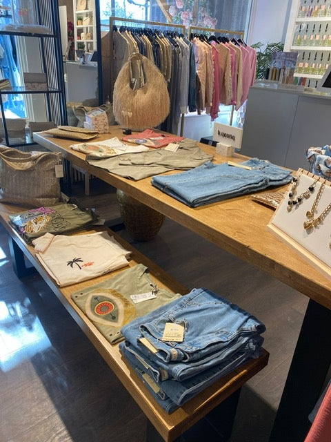 Grote presentatietafel winkel van Design85 met kleding, sieraden en tassen op twee houten niveaus.